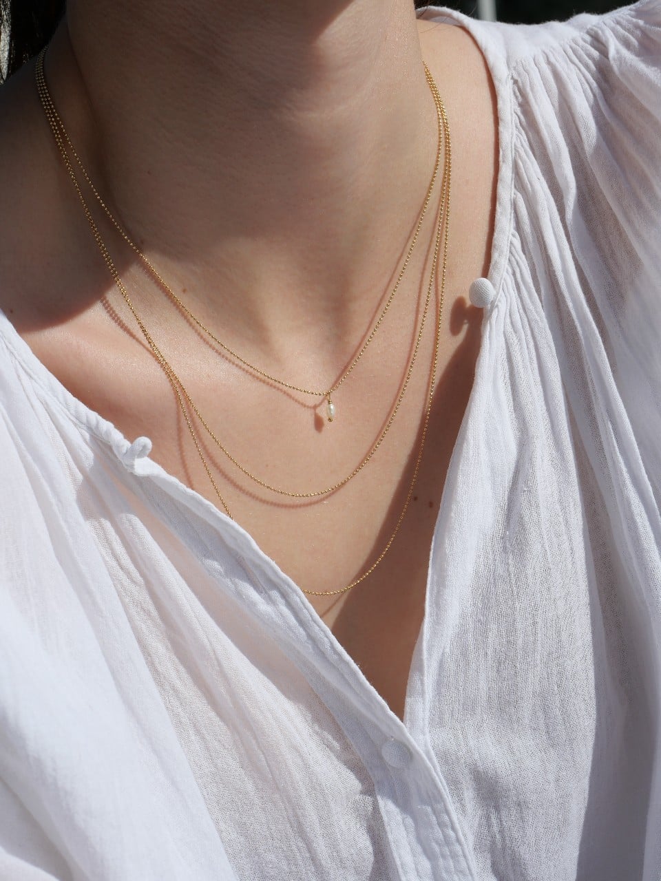 Collier Maggie 1 Collier Maggie triple rang en argent 925 plaqué or 3 microns, composé de trois chaînes fines de longueurs différentes. Bijou minimaliste et élégant porté sur une blouse blanche, fabrication française.