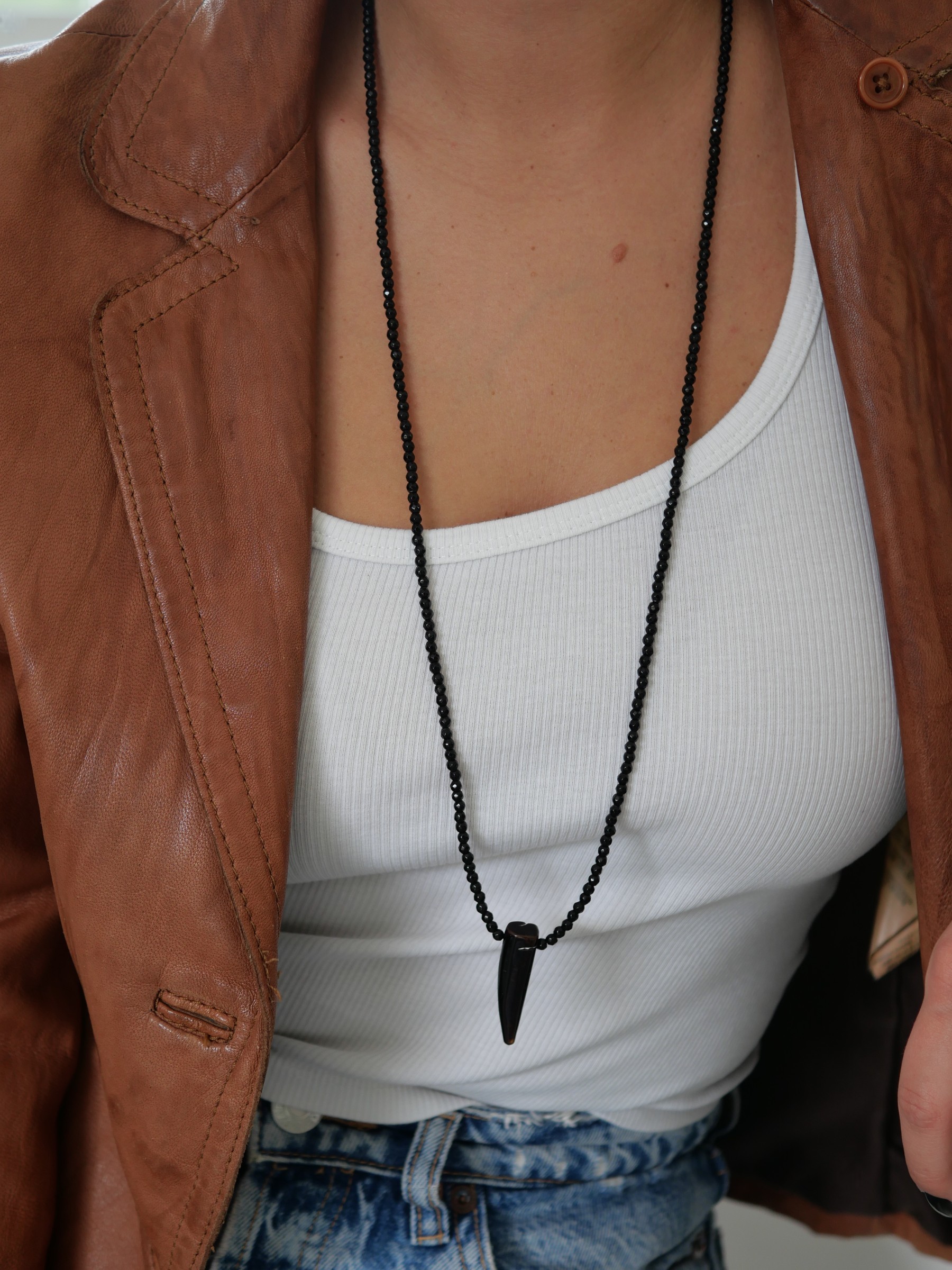 Sautoir Wild love 1 Sautoir Wild Love en perles d’onyx noir et pendentif corne en agate, porté sur un débardeur blanc avec une veste en cuir cognac — Loumaé Bijoux.