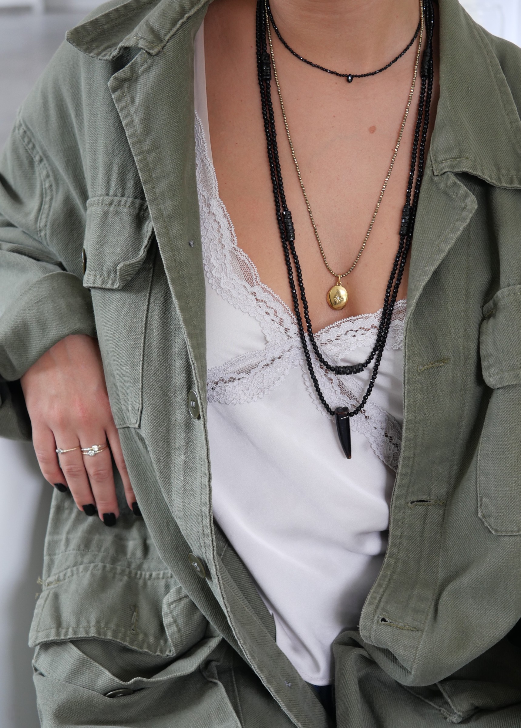 Collier Skinny Love 2 Collier Skinny Love en onyx noir porté en accumulation avec le collier Ninette et les sautoirs Black Betty et Wild Love, sur un top blanc et une chemise kaki.
