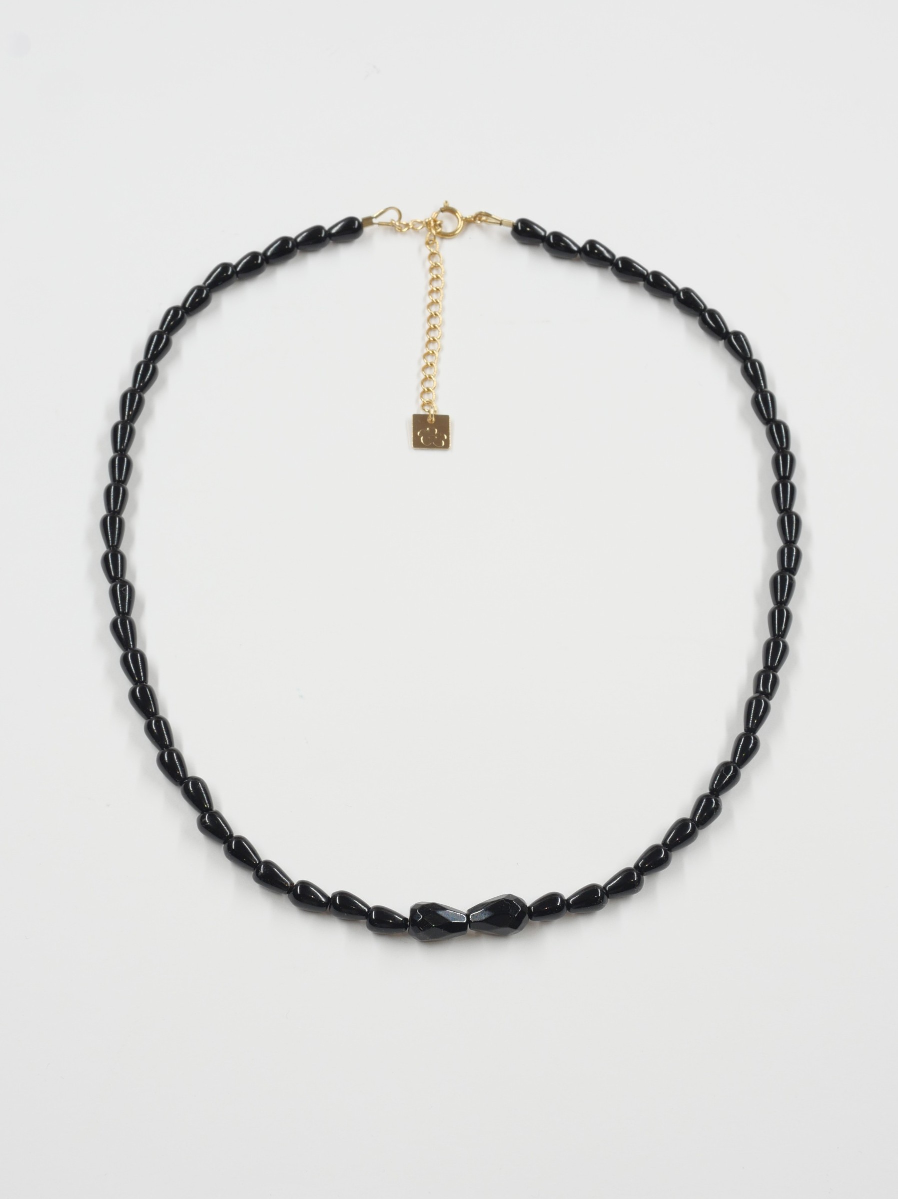 Collier Sweet rebel 4 Collier Sweet Rebel en onyx noir sur fond blanc, avec deux pierres centrales facettées, fermoir en or laminé et chaîne de rallonge.