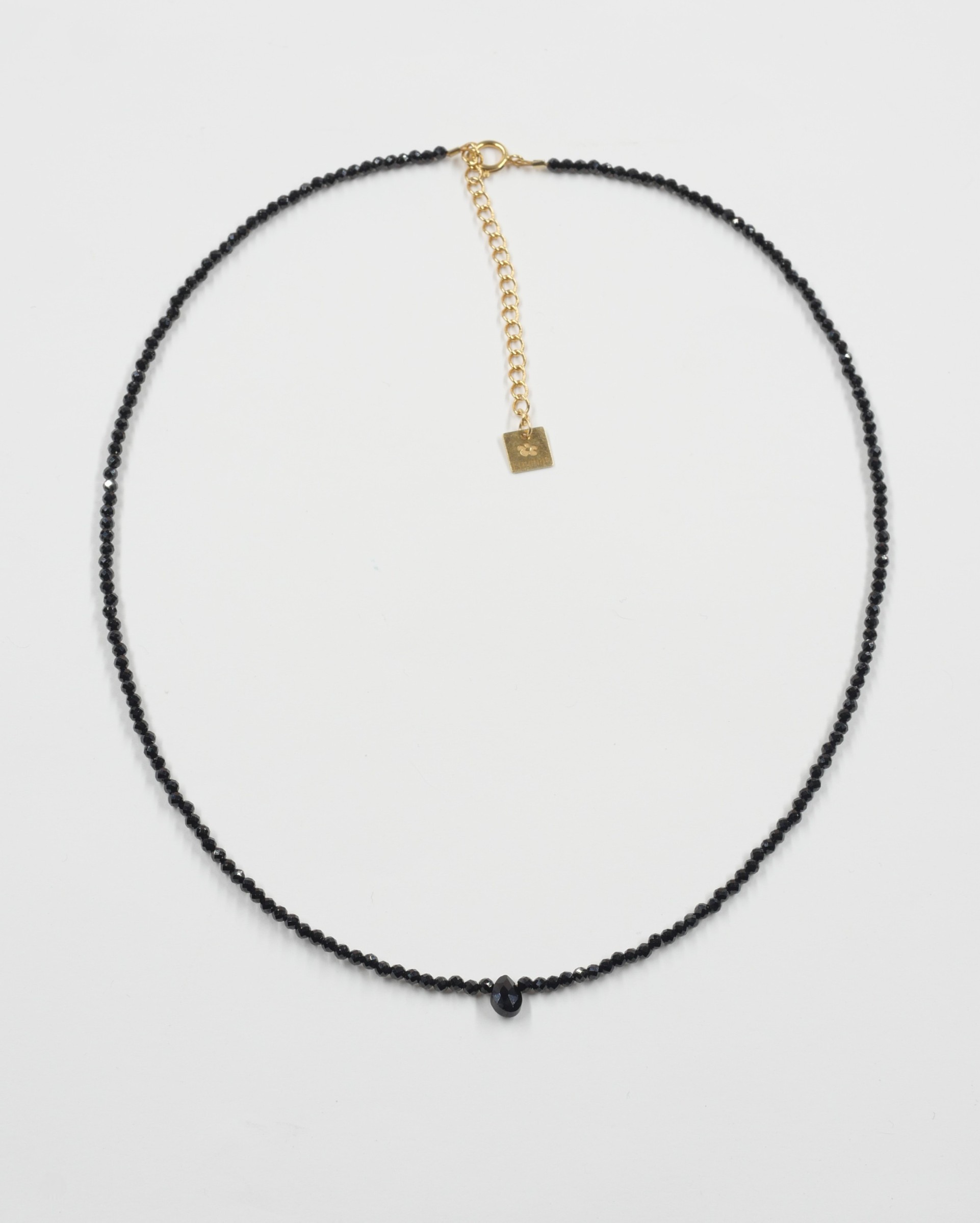 Collier Skinny Love 3 Collier Skinny Love en perles d’onyx noir facettées avec goutte centrale, fermoir et chaîne de rallonge dorés, présenté sur fond blanc.