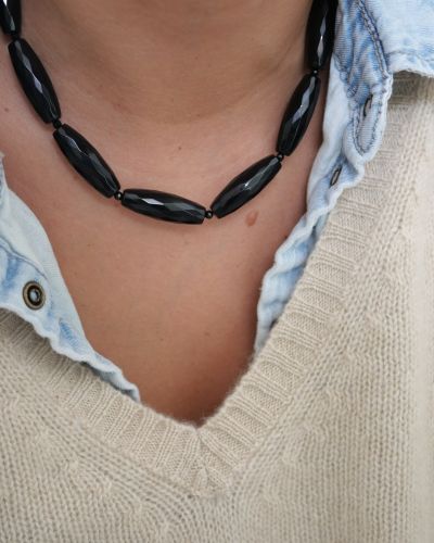 Collier Big Mama en pierres d’onyx noir facettées, porté au cou avec une chemise en jean et un pull crème — Loumaé Bijoux.