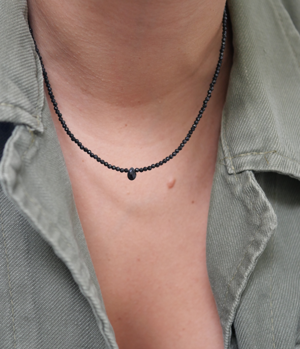 Collier Skinny Love en fines perles d’onyx noir facettées et goutte centrale, porté dans l’ouverture d’une chemise kaki.