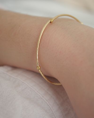 Bracelet Thaïs en or laminé (gold filled) porté au poignet, composé de tubes finement gravés et de petites perles dorées.
