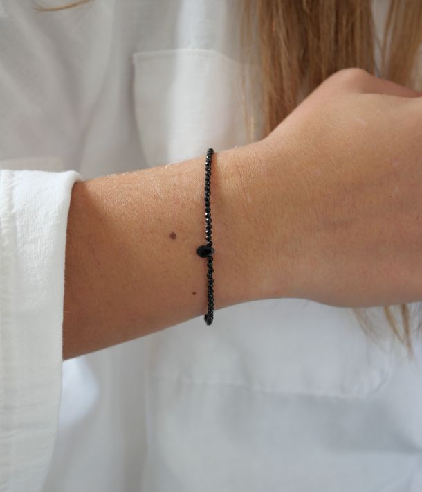 Bracelet Skinny Love en fines perles d’onyx noir facettées avec une petite goutte centrale, porté au poignet avec une chemise blanche.