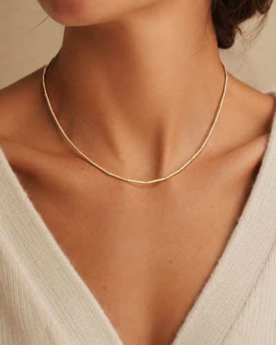 Collier Nova en tubes d’or laminé et perles en argent 925 porté avec un pull crème.