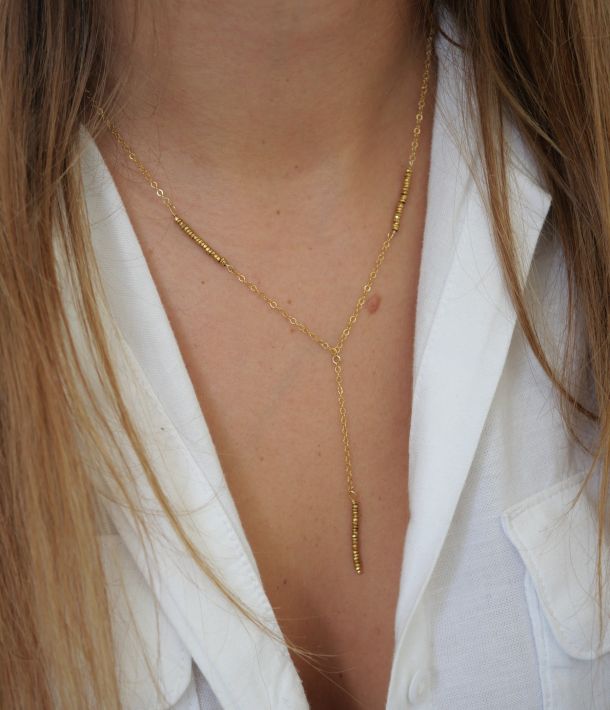 Collier Nikki 33 Collier Jane en or laminé et hématite dorée, porté sur la peau avec une chemise blanche ouverte.