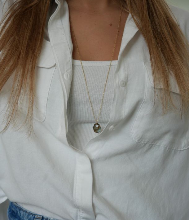 Collier Nikki 34 Sautoir Misty en argent 925 plaqué or 3 microns, avec pendentif ovale en labradorite aux reflets bleu-vert, porté sur une chemise blanche.