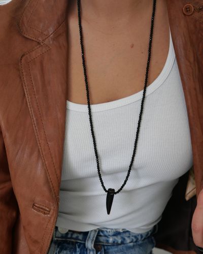 Sautoir Wild Love en perles d’onyx noir et pendentif corne en agate, porté sur un débardeur blanc avec une veste en cuir cognac — Loumaé Bijoux.