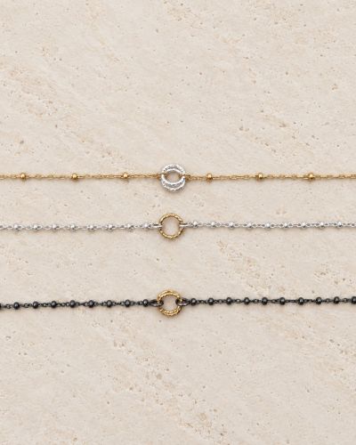 Trois bracelets Naty bicolores en or laminé, argent 925 recyclé et argent 925 recyclé rhodié noir sur travertin clair