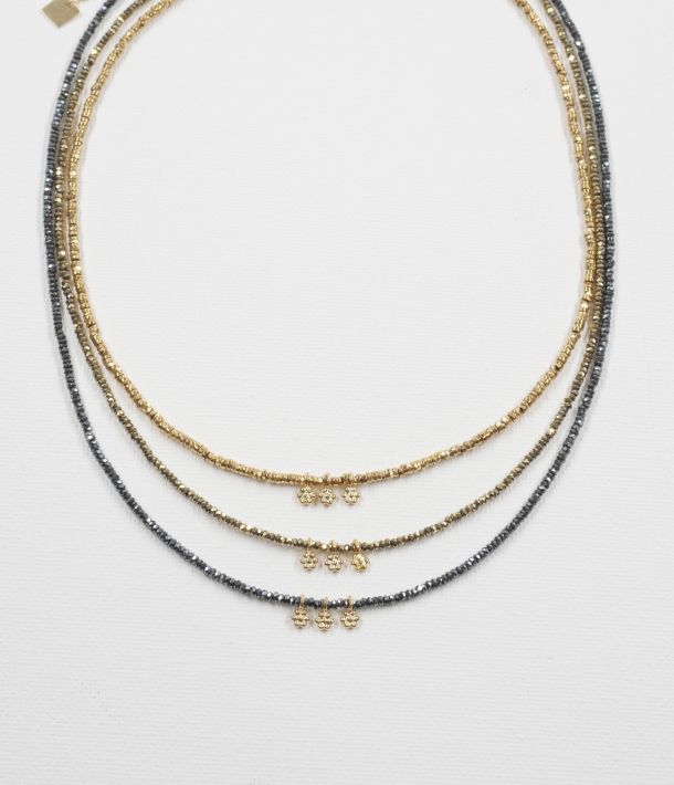 Trois colliers ras de cou Séléna en hématite facettée dorée, kaki et grise, chacun orné de trois petites fleurs dorées, présentés sur fond blanc.