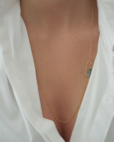 Bague Pearl 22 Collier long en or laminé avec épingle artisanale et perles turquoise porté sur un top blanc