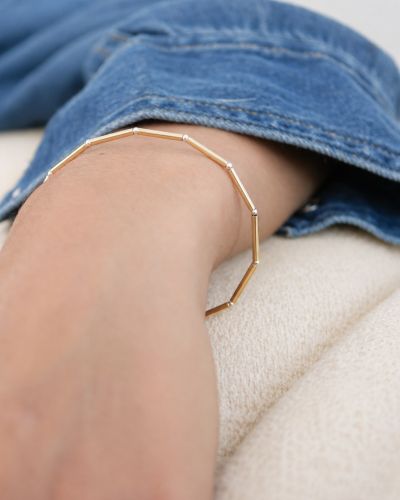 Bracelet Nova en tubes d’or laminé et petites perles en argent 925 porté au poignet avec une chemise en jean.