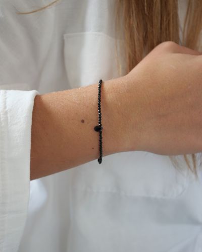 Bracelet Skinny Love en fines perles d’onyx noir facettées avec une petite goutte centrale, porté au poignet avec une chemise blanche.