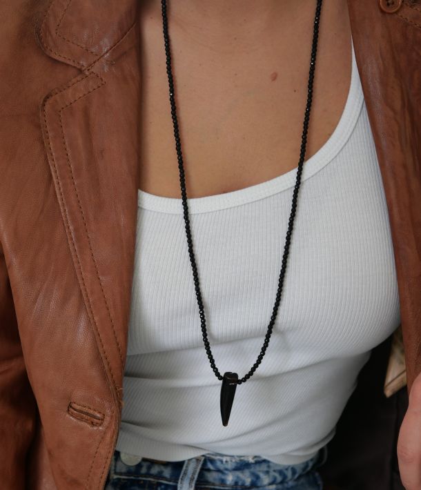 Sautoir Wild Love en perles d’onyx noir et pendentif corne en agate, porté sur un débardeur blanc avec une veste en cuir cognac — Loumaé Bijoux.