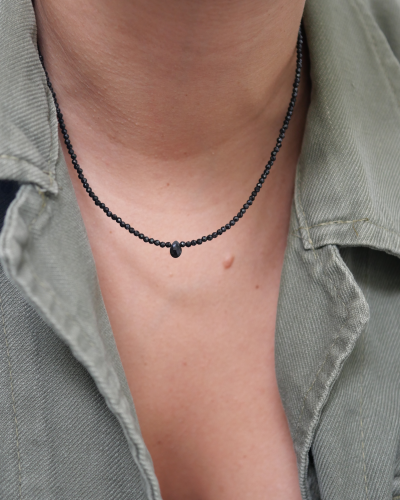 Collier Skinny Love en fines perles d’onyx noir facettées et goutte centrale, porté dans l’ouverture d’une chemise kaki.