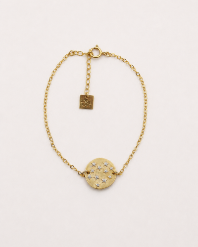 Bracelet Céleste en gold filled avec médaille dorée et étoiles en argent rhodié blanc, présenté à plat sur fond crème.